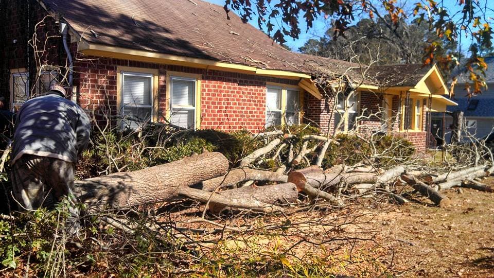 Storm-damaged oak fallen across a brick home — emergency tree removal job